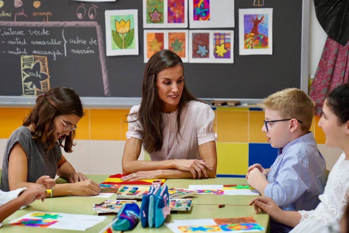 La Reina Letizia, sentada a una mesa del aula con dos alumnos y una profesora