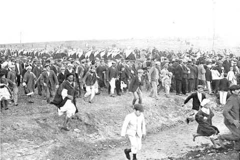 Una multitud corre por un campo abierto al paso de la comitiva real