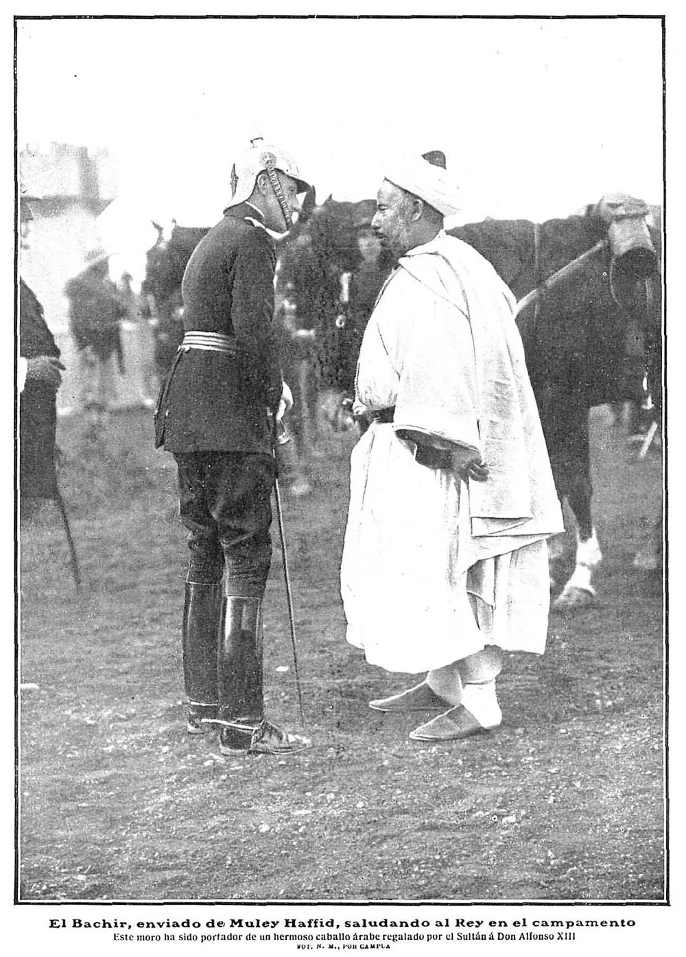 Alfonso XIII, de uniforme y casco de pincho, saluda a El Bachir, vestido de blanco