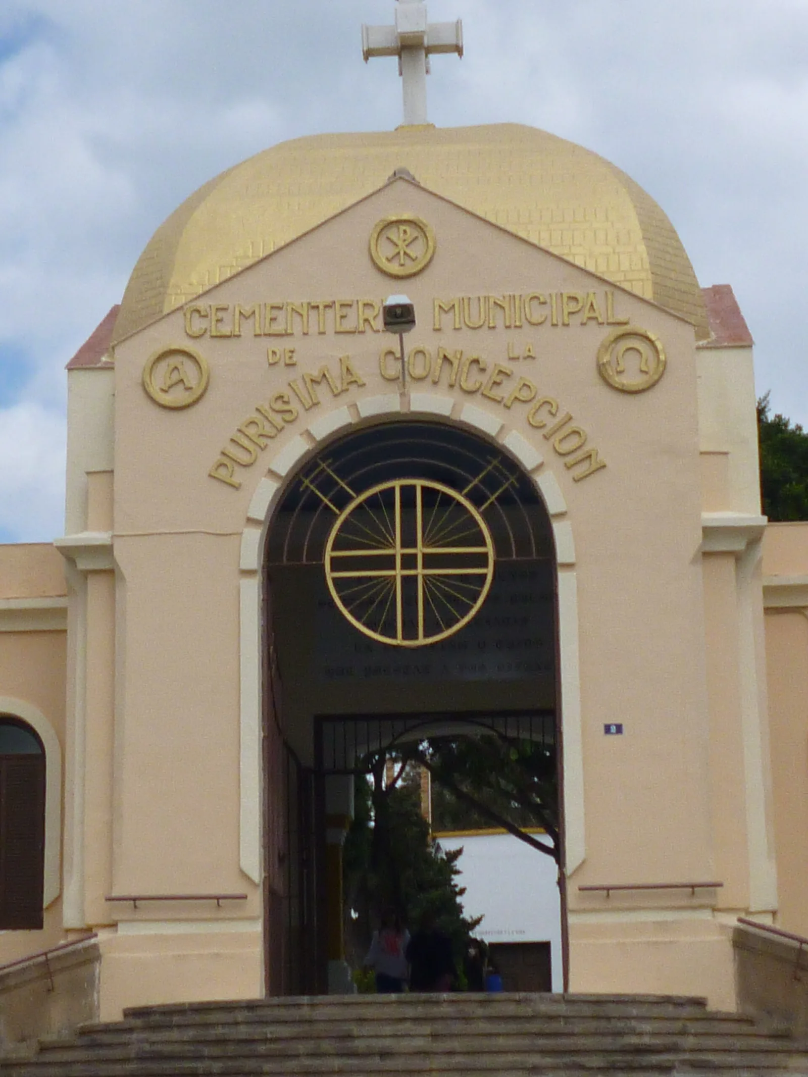 Pórtico de entrada del cementerio municipal de la Purísima Concepción de Melilla, con cúpula dorada, cruz y el nombre del cementerio en letras sobre el arco