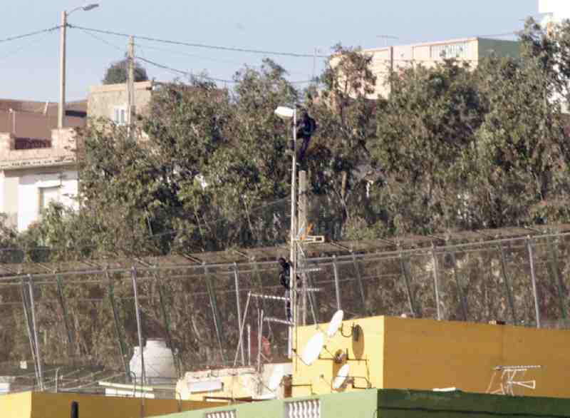 Dos inmigrantes se encaraman a un poste tras saltar la valla de Melilla