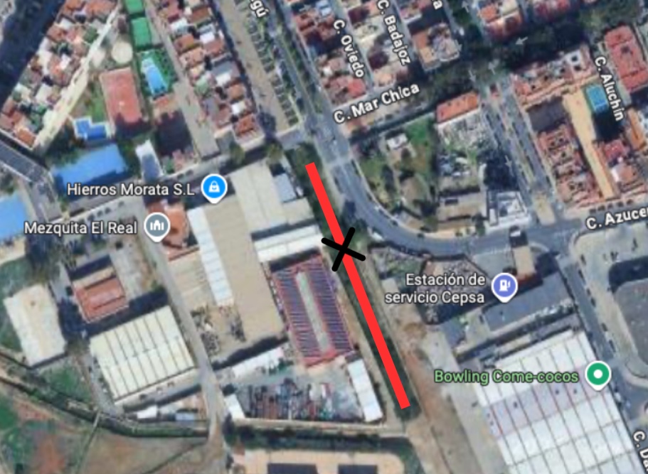 Vista aérea de una zona urbana con naves industriales, calles y una línea roja diagonal marcada con una X sobre una vía.
