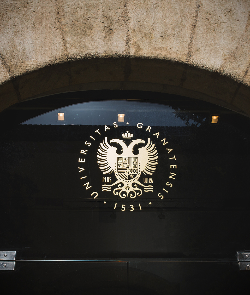Emblema circular dorado con águila bicéfala y escudo sobre una superficie negra bajo un arco de piedra.