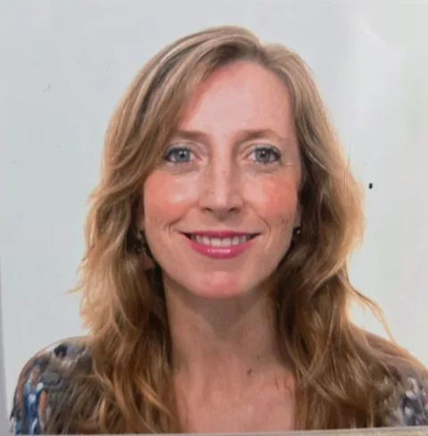 Primer plano de una mujer sonriente de pelo rubio ondulado y labios rosados, sobre fondo claro.