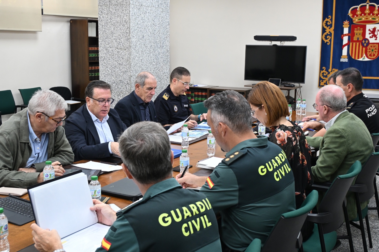 Varias personas sentadas alrededor de una mesa de reuniones, algunas con uniforme de la Guardia Civil, revisando documentos.